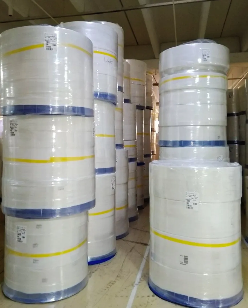 Stacked large rolls of white paper wrapped with blue and yellow bands in a warehouse.