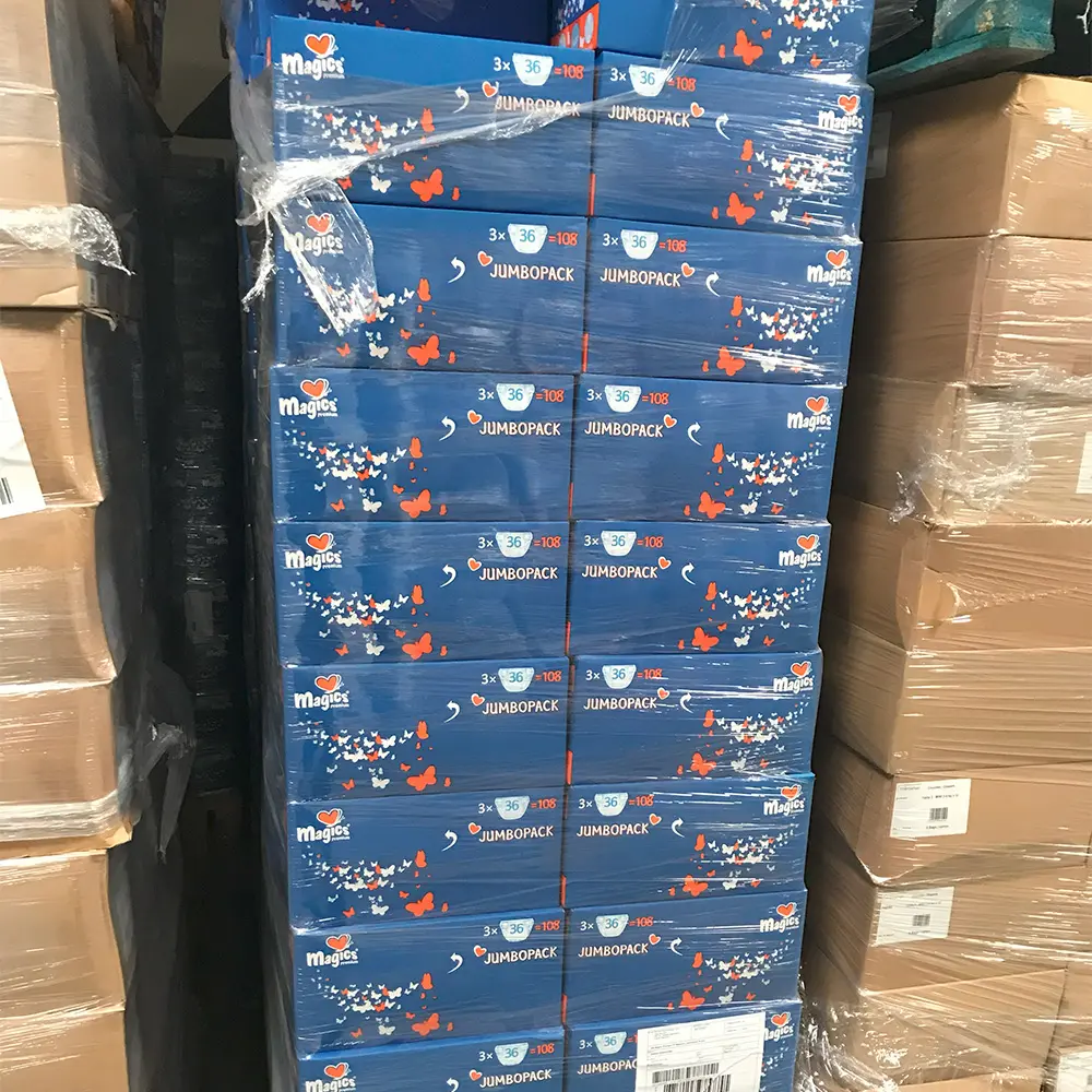 Stacked blue boxes of Magics brand diaper Jumbopacks wrapped in plastic on a warehouse pallet.